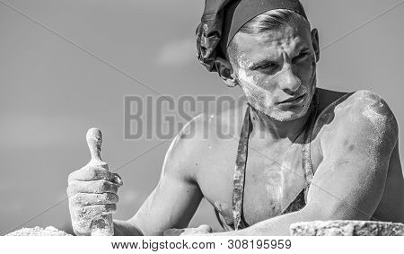 Man On Strict Face Wears Cooking Hat And Apron, Sky On Background. Cook With Sexy Torso Holds Rollin