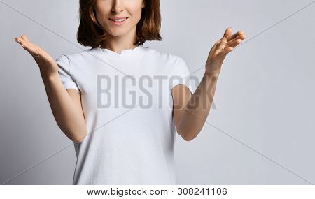 Young Smiling Woman In White T-shirt Shows Size Of Something Big With Her Arms With Open Palms On Wh