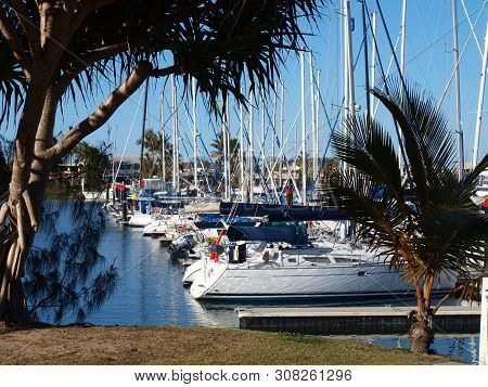 Nautical Waterscape With Boats Berthed At A Tropical Waterfront Marina Including Palm Trees And Blue