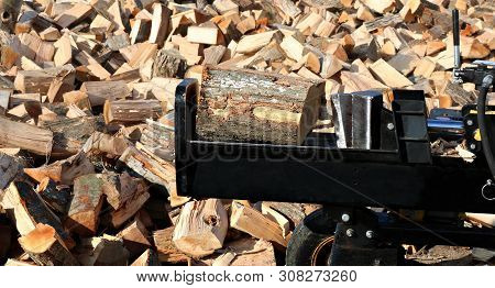 Closeup Of Wood Splitter Blade About To Slice Through Block Of Firewood With Split Pieces Piled All 