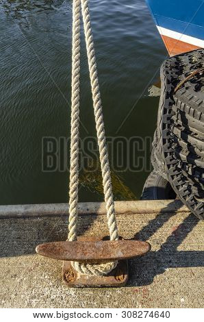 Line And Rusty Horn Cleat Securing Bow Of Fishing Boat To Dock