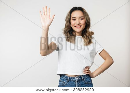 Portrait of a lovely young asian woman standing isolated over white background, waving hand