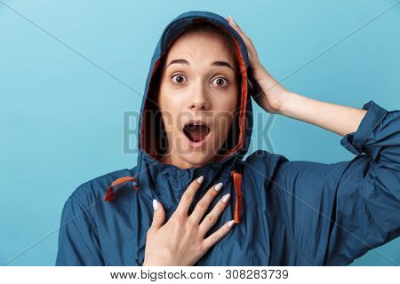 Cheerful young girl wearing raincoat standing isolated over blue background, posing