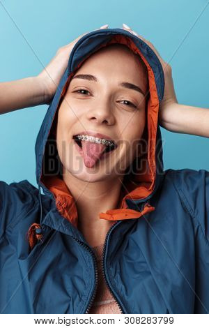 Cheerful young girl wearing raincoat standing isolated over blue background, posing
