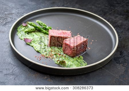 Blanched green asparagus tips with barbecue dry aged wagyu fillet steak and avocado coriander relish as closeup on a modern design plate