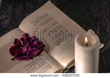 An Open Book With A Candle. On The Pages Is A Bud Of Dried Rose.