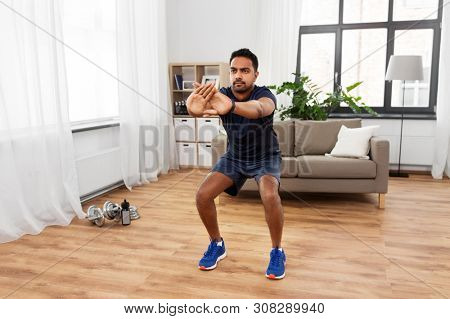 sport and healthy lifestyle concept - indian man with fitness tracker exercising and doing squats at home
