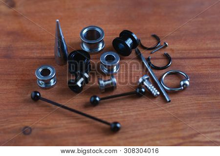 Jewelry Piercing Set. Piercing Accessories On Wooden Background. Stretching For Ear Tunnels , A Cath
