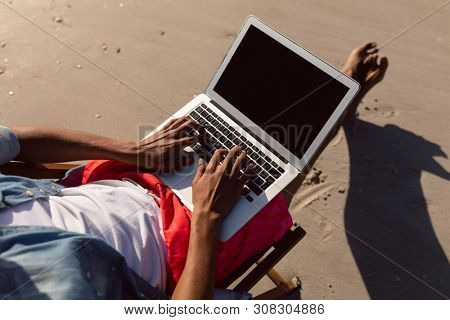 Low section of African-american man using laptop while relaxing in a beach chair on the beac