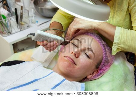A Young Girl Is Lying On Couch With A Pink Hat On Her Hair While Performing An Ultrasonic Face Clean
