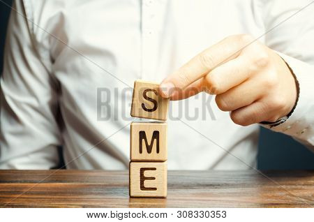 Businessman Holds Wooden Blocks With The Word Sme. Small And Medium-sized Enterprises - Commercial E
