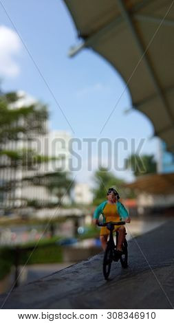 Close Up Mini Figure Woman Toys Bicycling At Building Gate With Negative Or Copy Space For Text Area