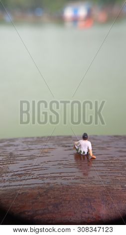 Mini Figure Toy Old Man Sit At Scratch Wooden Balcony At River Side With Copy Or Negative Space For 
