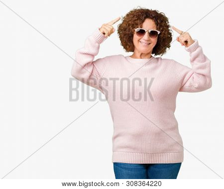 Beautiful middle ager senior woman wearing pink sweater and sunglasses over isolated background Smiling pointing to head with both hands finger, great idea or thought, good memory
