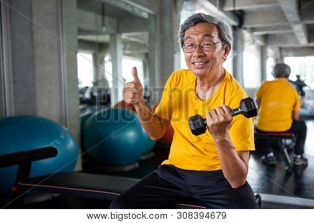 Senior Asian Sport Man Lifting Dumbbells And Show Thumbs Up In Fitness Gym . Elder Male Exercising ,