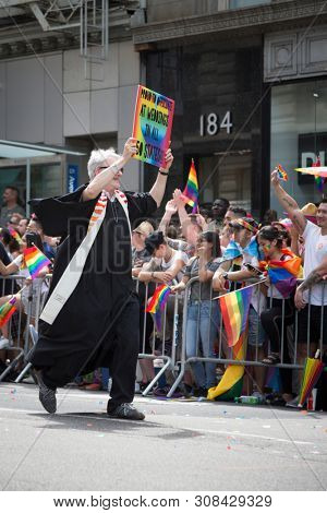 2018 JUNE 24 NEW YORK: NYC Pride March participant holds a rainbow sign that says Proud To Officiate At Weddings In All 50 States on the 5th Ave parade route.