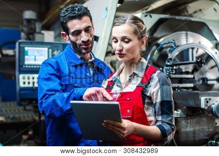 Woman and man manufacturing worker in discussion writing on tablet computer 