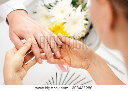 Pedicurist looking at fingernails of man prior to manicure in her studio 