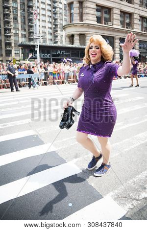 2018 JUNE 24 NEW YORK: NYC Pride March participant wearing a purple sequined dress outfit waves to the crowd along the 5th Ave parade route.