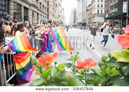 2018 JUNE 24 NEW YORK: Two NYC Pride March participants run together holding hands past cheering spectators on the 5th Ave parade route.