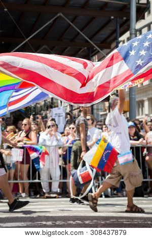 2018 JUNE 24 NEW YORK: NYC Pride March participant walks with an American Flag at 23rd St and 5th Ave on the parade route.