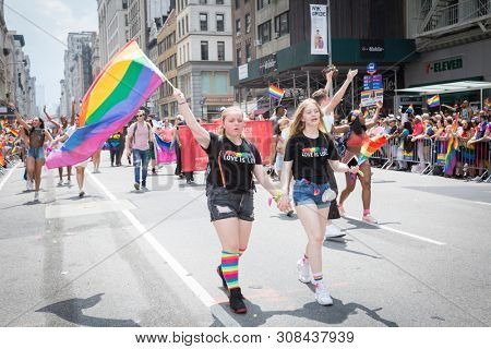 2018 JUNE 24 NEW YORK: Two NYC Pride March participants walk together holding hands wearing rainbow colored tshirts on the 5th Ave parade route.
