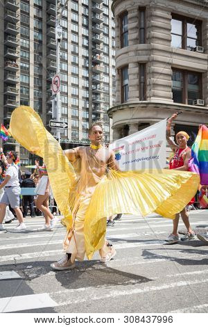 2018 JUNE 24 NEW YORK: NYC Pride March participant wearing a gold outfit with wings walks along the 5th Ave parade route.