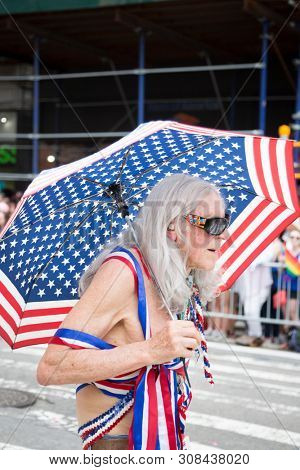 2018 JUNE 24 NEW YORK: NYC Pride March participant walks with an American Flag umbrella at 23rd St and 5th Ave on the parade route.