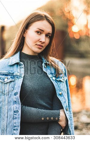Portrait Of The Attractive, Slender, Beautiful Young Caucasian Blonde Girl In A Jeans Jacket. Smilin