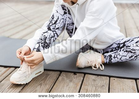 Close up of a sportswoman tying shoelace while sitting on a fitmess mat outdoors