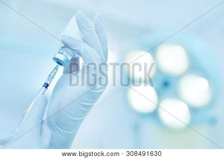 Hand Holding Syringe And Medicine Vial Prepare For Injection In Operating Room With Surgery Lamp Bac