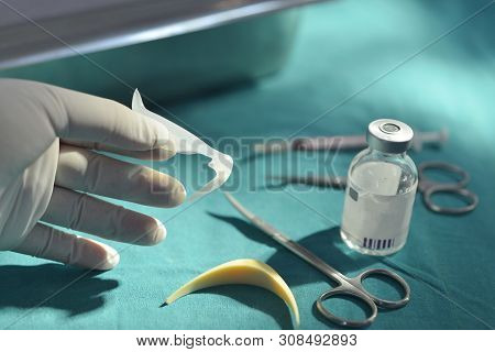 Hand Holding Silicone Nasal Implant In Operating Room With Surgical Equipment And Medicine Vial Back