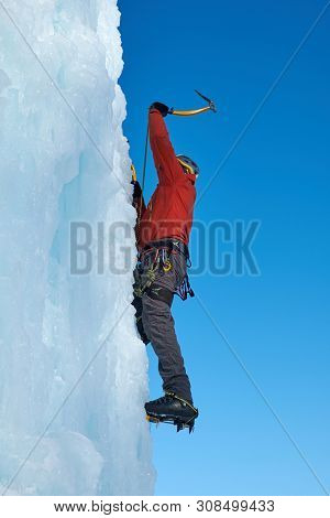 Ice-climber Man With Ice Tools Axe Climbing A Large Wall Of Ice. Ou