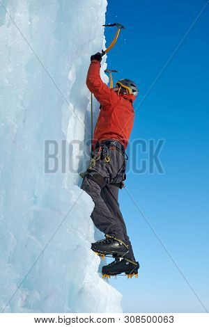 Alpinist Man With Ice Tools Axe Climbing A Large Wall Of Ice. Outdoor Sports Portrait.