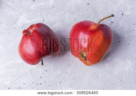 Close-up Two Ugly Red Apples On Grey Concrete Background.