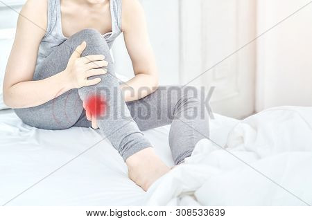 Asian Girl Wearing Gray Dress Have Leg Pain. The Woman Was Squeezing Her Leg In A White Bedroom With