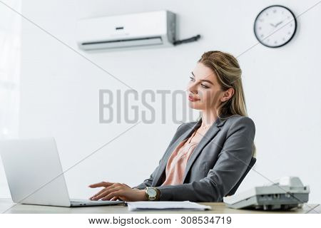 Happy Businesswoman Sitting In Office With Air Conditioner And Usinglaptop