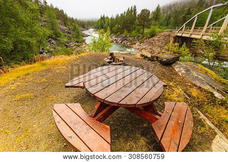 Rest Area Wooden Table With Benches At Mountain River, Norwegian Green Nature In Summertime. Cloudy 