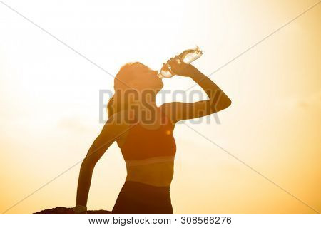 Young Woman Resting and Drinking Water after Trail Running Outdoor. Workout Exercise at Hot Beautiful Summer Sunset. Sport and Healthy Active Lifesyle Concept.
