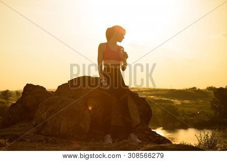 Young Woman Resting and Drinking Water after Trail Running Outdoor. Workout Exercise at Hot Beautiful Summer Sunset. Sport and Healthy Active Lifesyle Concept.