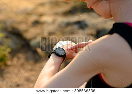 Young Woman Runner Using Multisport Smartwatch at Sunset on the Mountain Trail. Closeup of Hands with Fitness Tracker. Training and Sports Concept.