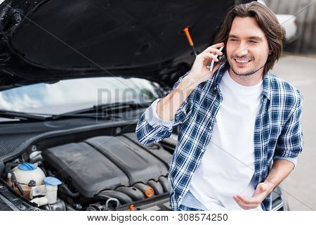 Cheerful Man In Casual Cothes Talking On Smartphone Near Broken Auto With Open Trunk, Car Insurance 