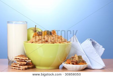 leckere Cornflakes in grüne Schale, Äpfel und Glas Milch auf Holztisch auf blauem Hintergrund
