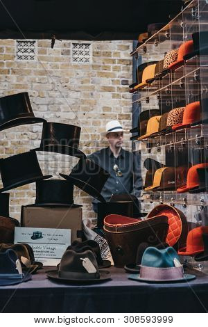 London, Uk - June 22, 2019: Man Behind Hats On Sale At A Stall Inside Spitalfields Market, One Of Th