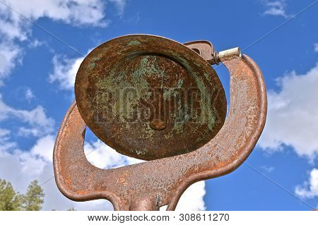 Looking Into The Underside Of An Old Huge Copper Bell  Upheld By A Strong Rusty Support Frame.