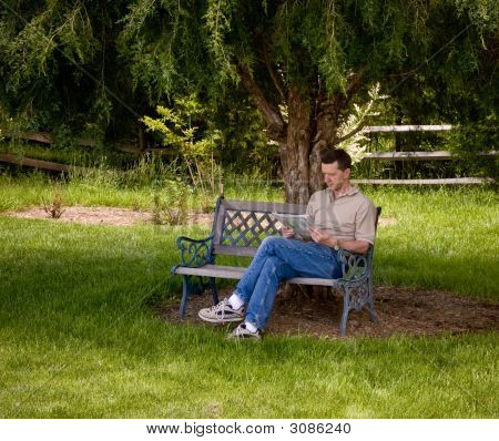 Muž čtení novin pod stromem