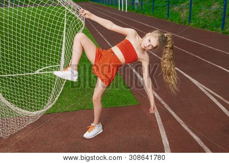 A full lenth portrait of a sporty teenager girl posing on the sports ground near the net. Sport fashion, active lifestyle.