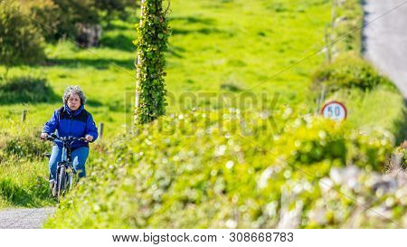 Tired Mature Mexican Woman Riding Her Bicycle Among The Meadows Of A Hill, Expression On Her Face, E