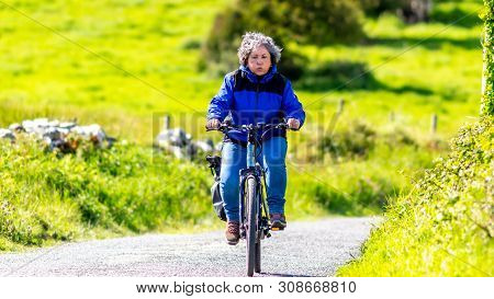 Tired Mature Mexican Woman Driving Her Bicycle On A Hill, Expression On Her Face, Exhaling Air, Wond