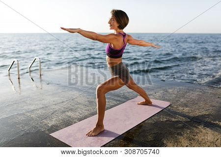 Woman With Dark Short Hair Standing And Pulling Hands Aside While Training Yoga Poses By The Sea